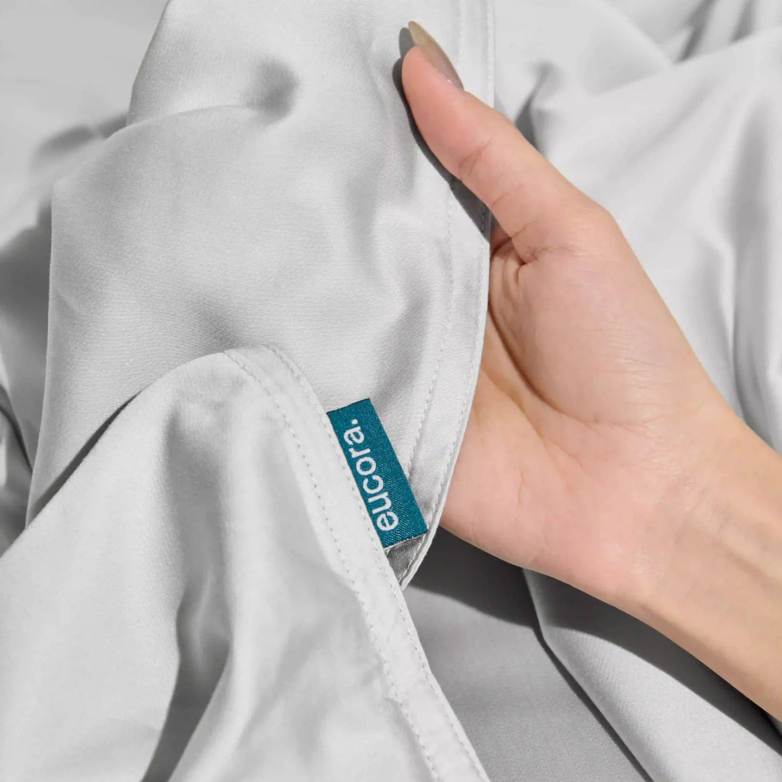 and holding corner of silky eucalyptus bamboo bed sheet showing soft weave and premium quality. Eco-friendly, breathable bamboo bedding material.