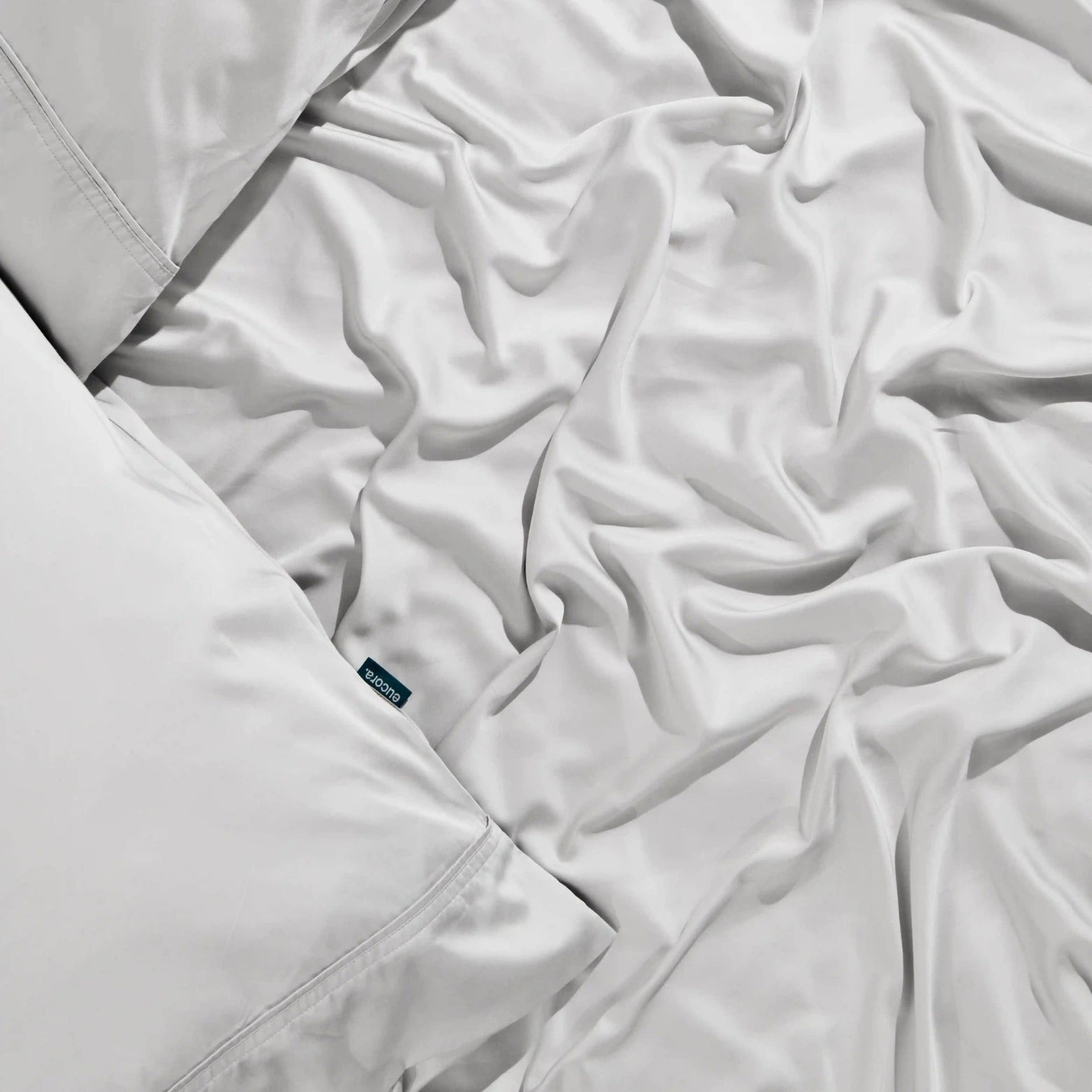 Hand adjusting white eucalyptus bamboo bed sheet with premium label. Ethically made from organic bamboo viscose for silky, sustainable comfort.